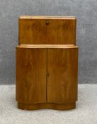 A mid century Art Deco style walnut cocktail or drinks cabinet having a shaped fall front opening on