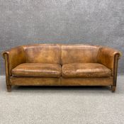 A mid century distressed tan leather Chesterfield style sofa having a scrolled back and arms with