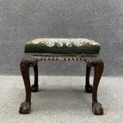 A Georgian style mahogany footstool having a stuffover needlework seat raised on carved acanthus