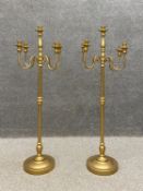 A pair of contemporary simulated brass floor standing candelabra each having four scrolling branches