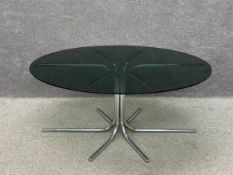 A mid to late 20th century dining table having an oval smoked glass top raised on a pedestal of
