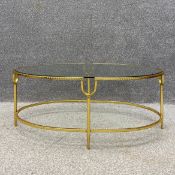 A contemporary coffee table having an oval plate glass top set into a shaped brass frame raised on