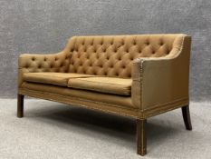 An early 20th century two seater sofa having a square button back and shaped arms over a cushioned