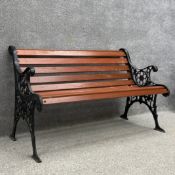 A contemporary 19th century style garden bench with scrolling openwork cast iron ends united by teak