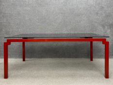 A contemporary dining table having a square smoked plate glass top floating above a red square