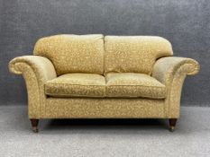 A Victorian style two seater sofa having a curved back with scrolled arms over a cushioned seat
