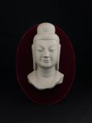 A 20th century Chinese ceramic tourist Buddha bust mounted to a red velvet plaque with a label to