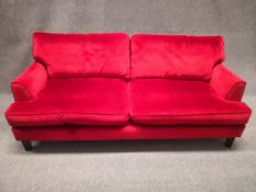 A contemporary three seater sofa having a cushioned back and seat upholstered in a red velour raised
