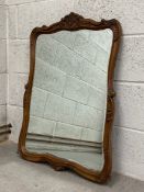 A 19th century French oak mirror having a ornately carved and shaped frame with a scrolling cresting