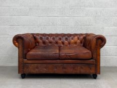 A 20th century tan leather Chesterfield two seater sofa having a scrolled button back and arms