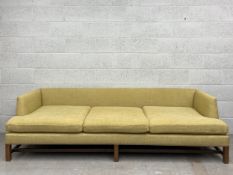 A mid-century style three seater sofa having square back and arms over a cushioned stuffover seat
