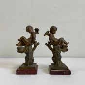 A pair of 19th century cold painted spelter figural putti figures raised on square stone plinth