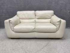 A contemporary Italian off-white leather two seater sofa having a cushioned back and arms with a