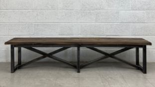 A contemporary industrial distressed teak refectory style bench having a heavy plank top raised on a