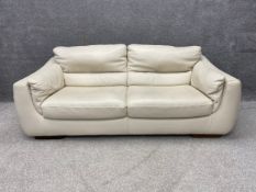 A contemporary Italian off-white leather two seater sofa having a cushioned back and arms with a