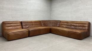 A vintage style tan leather modular corner sofa and matching footstool in the style of Timothy