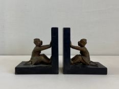 A pair of 20th century ebonised bookends each being supported by a mythological bronze monkey figure