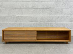 A contemporary oak tv or HiFi stand having a long rectangular top over two slatted sliding doors