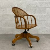 A vintage oak captains desk or office armchair having a curved rattan and spindle back and arms on a