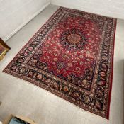 A large signed Persian carpet with central floral medallion on a burgundy field within foliate