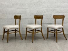 A set of three vintage style dining chairs each having a curved top rail with a white leather