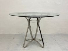 A contemporary dining table having a circular toughened glass top raised on a bent chrome