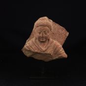 An Indian possibly Gupta period carved red sandstone figural bust in relief raised on a museum style