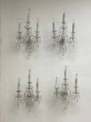 A set of four cut glass wall sconces each having three scrolling branches draped with cut glass