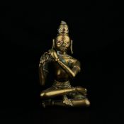 A 19th century Indian brass figural statue depicting a seated Krishna playing a flute inset with