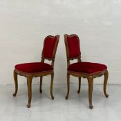 A pair of Louis XV style walnut dining chairs each having a carved and shaped back over a red velour