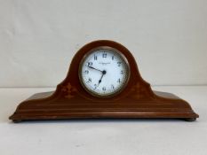An early 20th century mahogany mantle clock having a shaped and arched case with a feather-banded