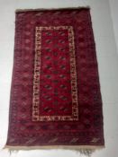 An Afghan Turkoman rug having two rows of nine guls over a burgundy ground within multiple