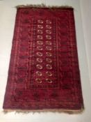 An Afghan Turkoman carpet having two rows of eleven guls over a burgundy ground within multiple