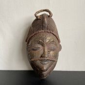 A West African carved wood tribal Punu mask from Gabon with an applied sheet of hammered brass