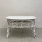 A vintage painted white wicker coffee table having an oval top with a woven openwork apron raised on