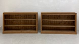 A pair of contemporary 19th century style low open pine bookcases each having a plank top over three