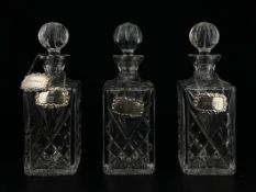 A set of three cut glass decanters each having a spherical stopper over a square body with a