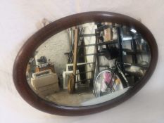An Edwardian mahogany wall mirror having an oval plate in an ebony and satinwood inlaid surround.