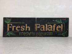 A hand painted sign, advert for 'Fresh Falafel', painted as a diptych across two large boards with