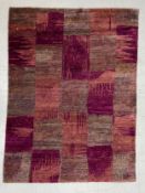 A vintage carpet decorated all-over with irregular panels and abstract designs in shades of pink and