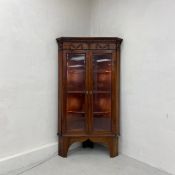 A 19th century style teak corner display cabinet having a dentil moulded cornice with a carved