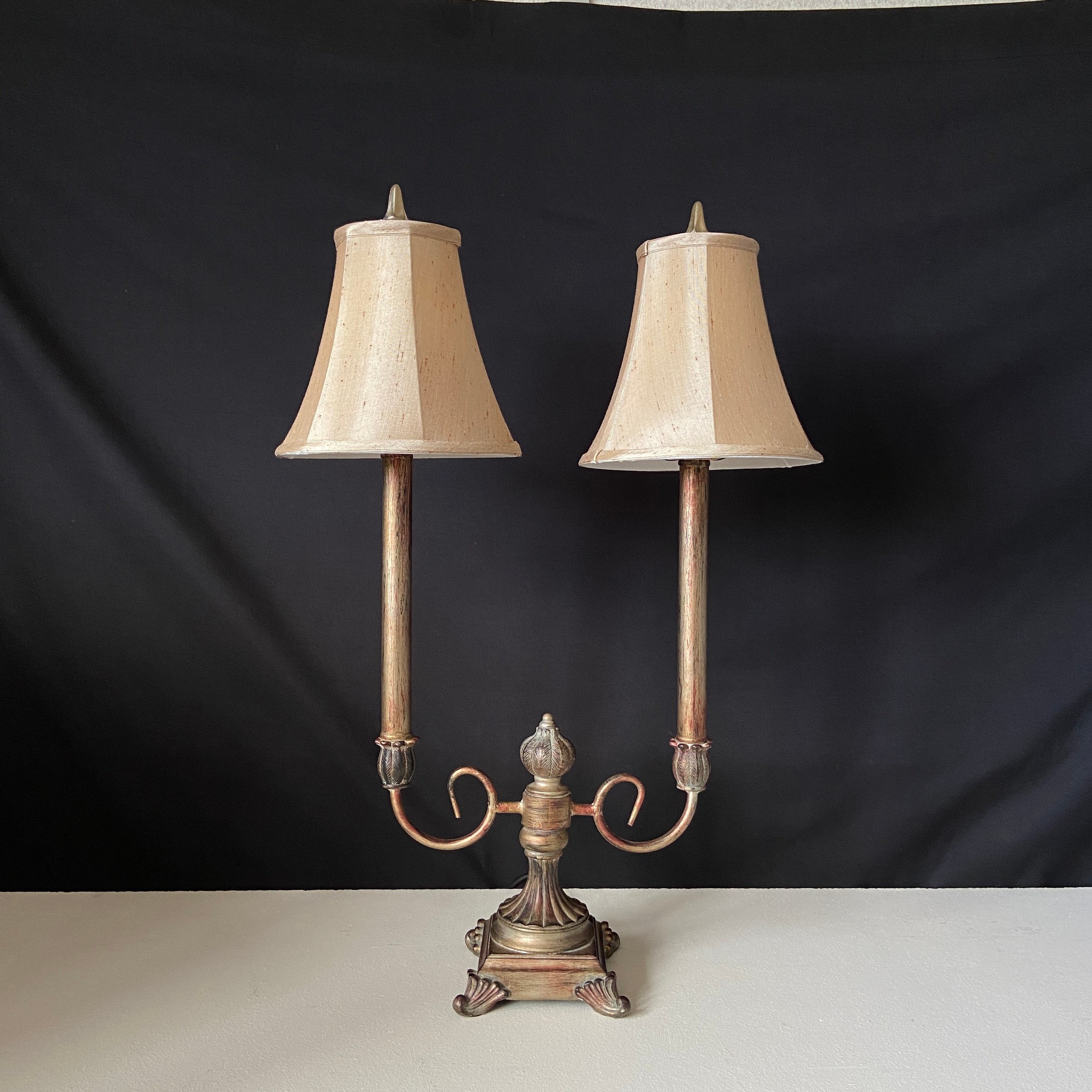 A contemporary cold painted and distressed metal candelabra style table lamp having two branches