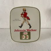A vintage Johnny Walker tin desktop calendar having a figure in dress with raised red lettering over