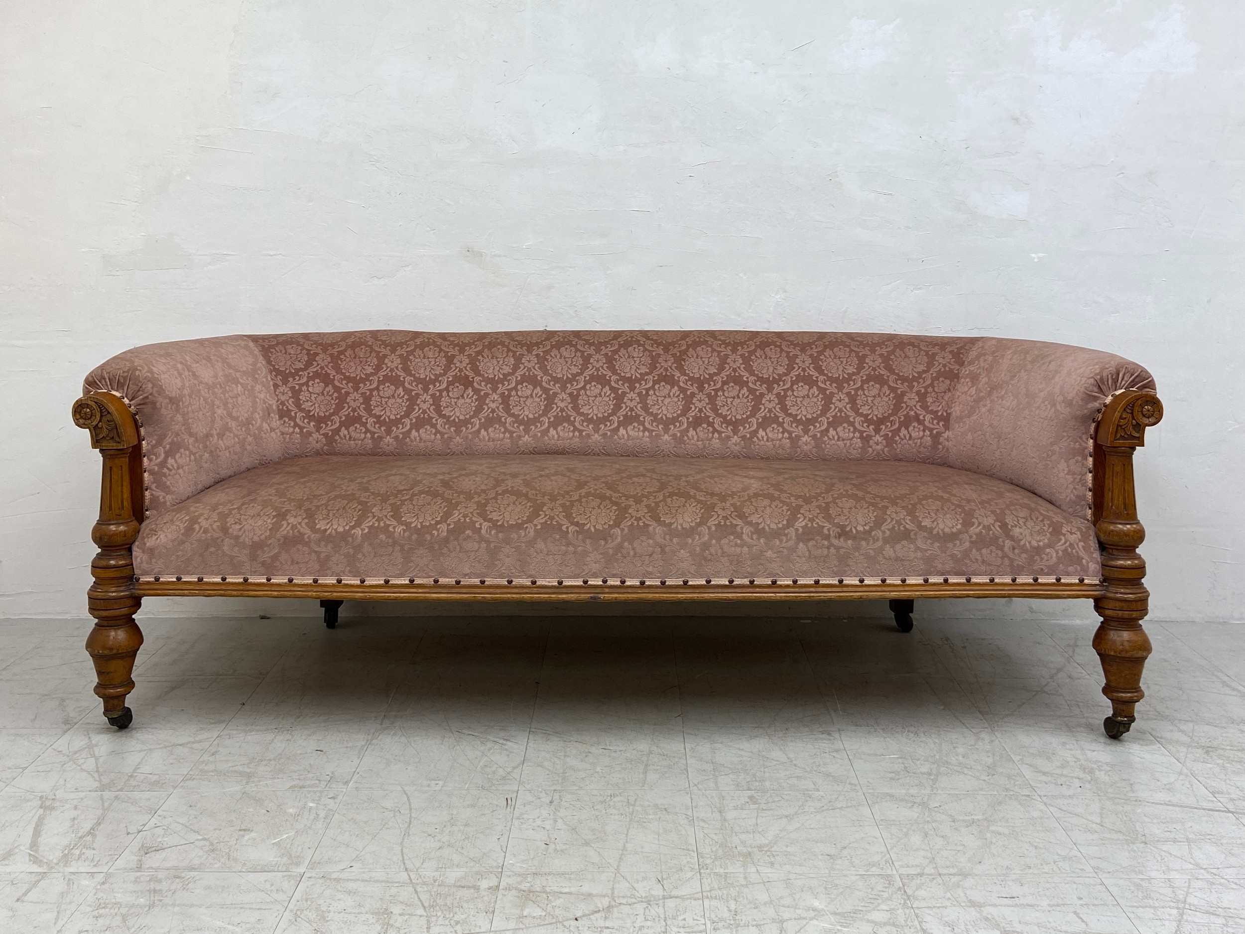 A mid 19th century oak sofa re-upholstered in foliate dusty pink raised on turned and carved