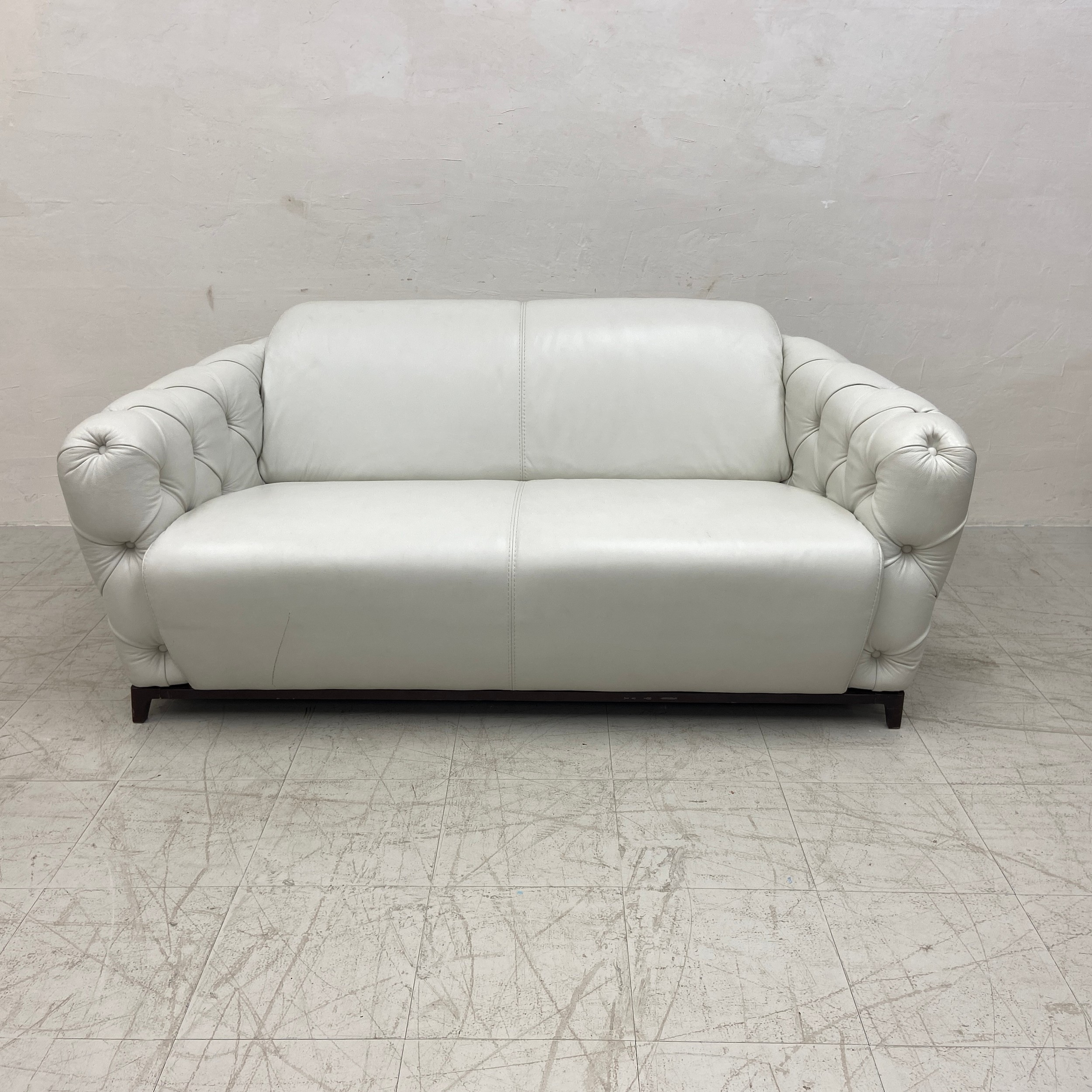 A contemporary Italian white leather two seater sofa having a curved back and deep buttoned arms