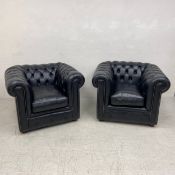 A pair of Chesterfield armchairs upholstered in black leather each having a scrolled deep button