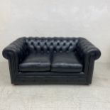 A black leather two seater Chesterfield sofa having a scrolled deep button back and arms over a