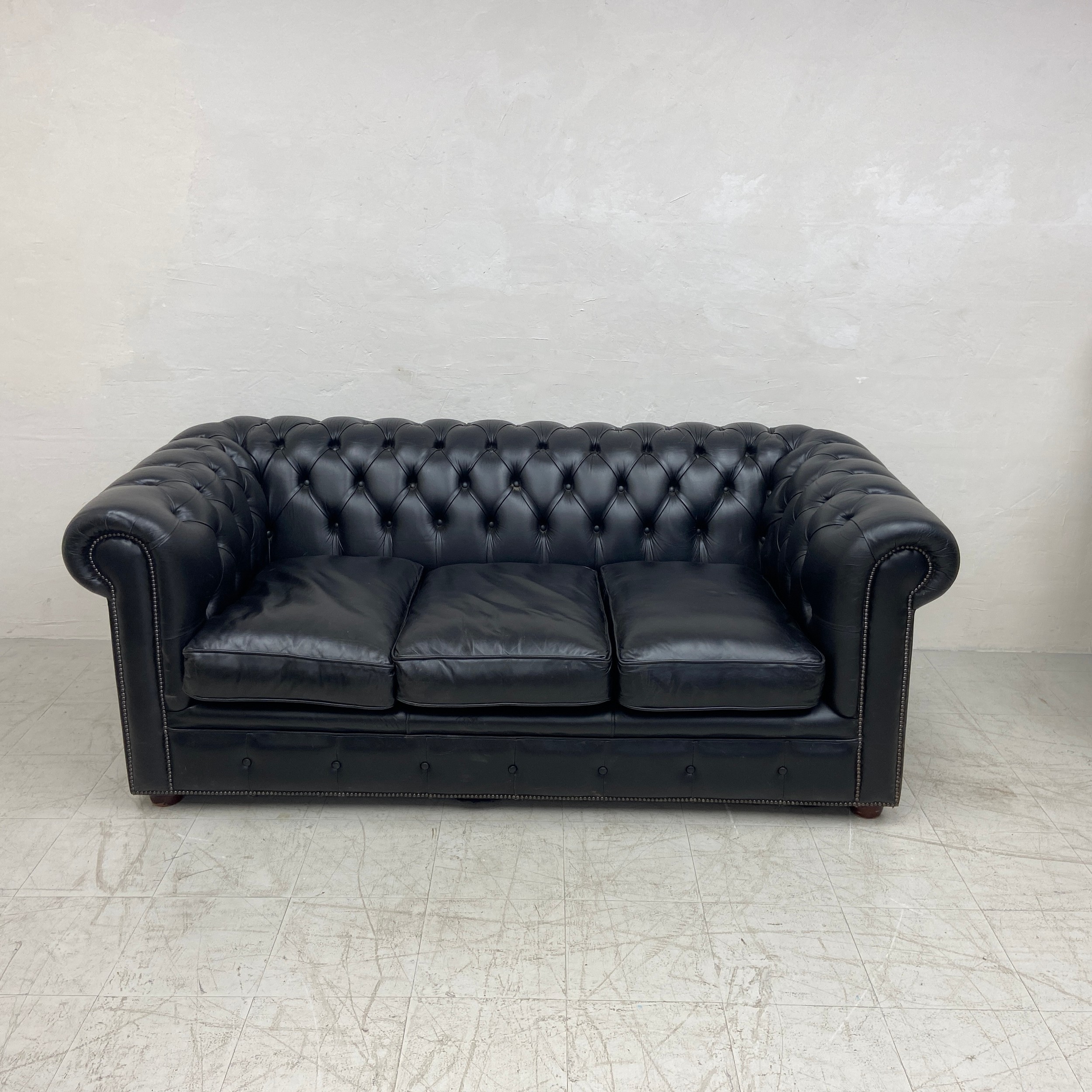 A black leather three seater Chesterfield sofa having a scrolled deep button back and arms over a