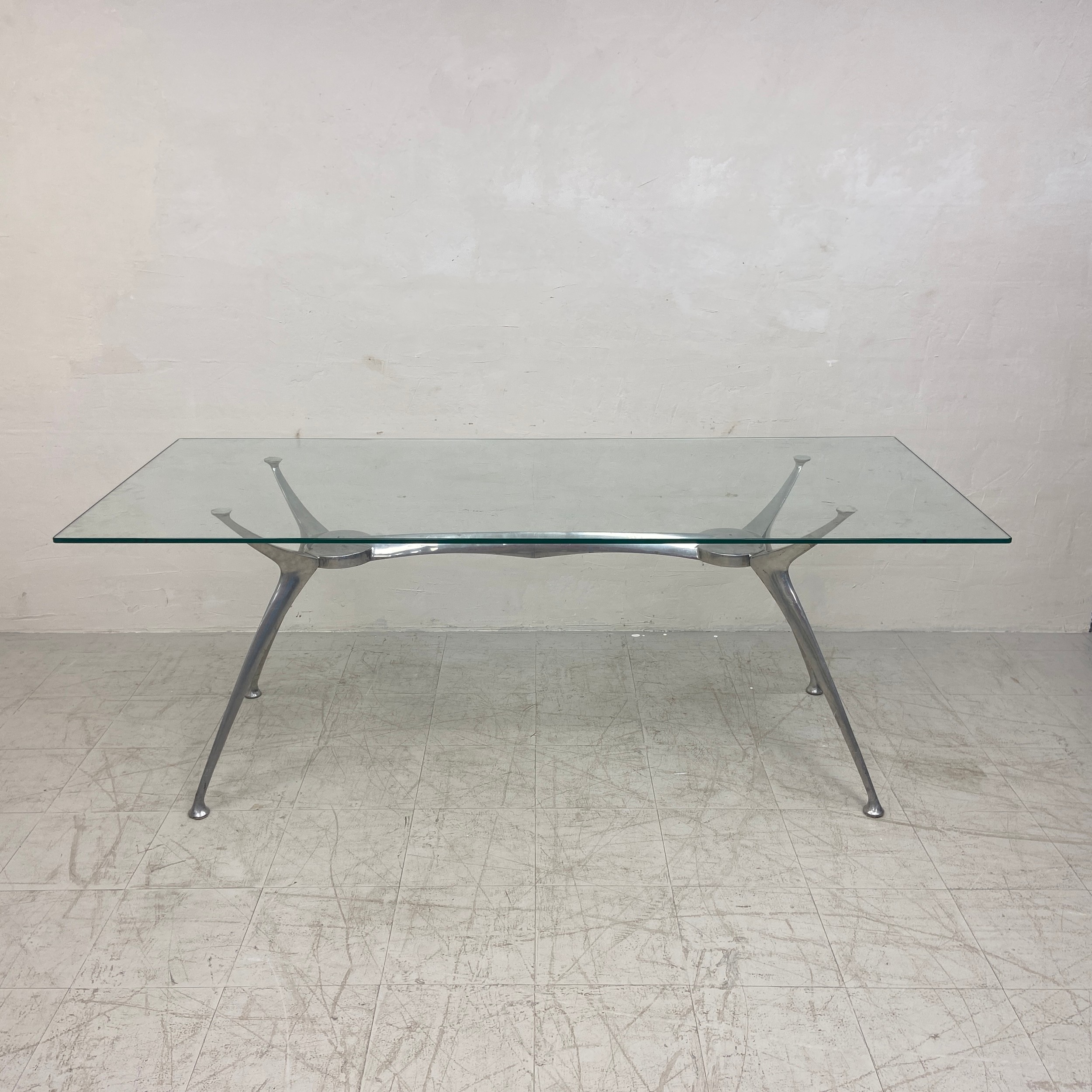A contemporary dining table in the style of Philippe Starck with plate glass top on an aluminium