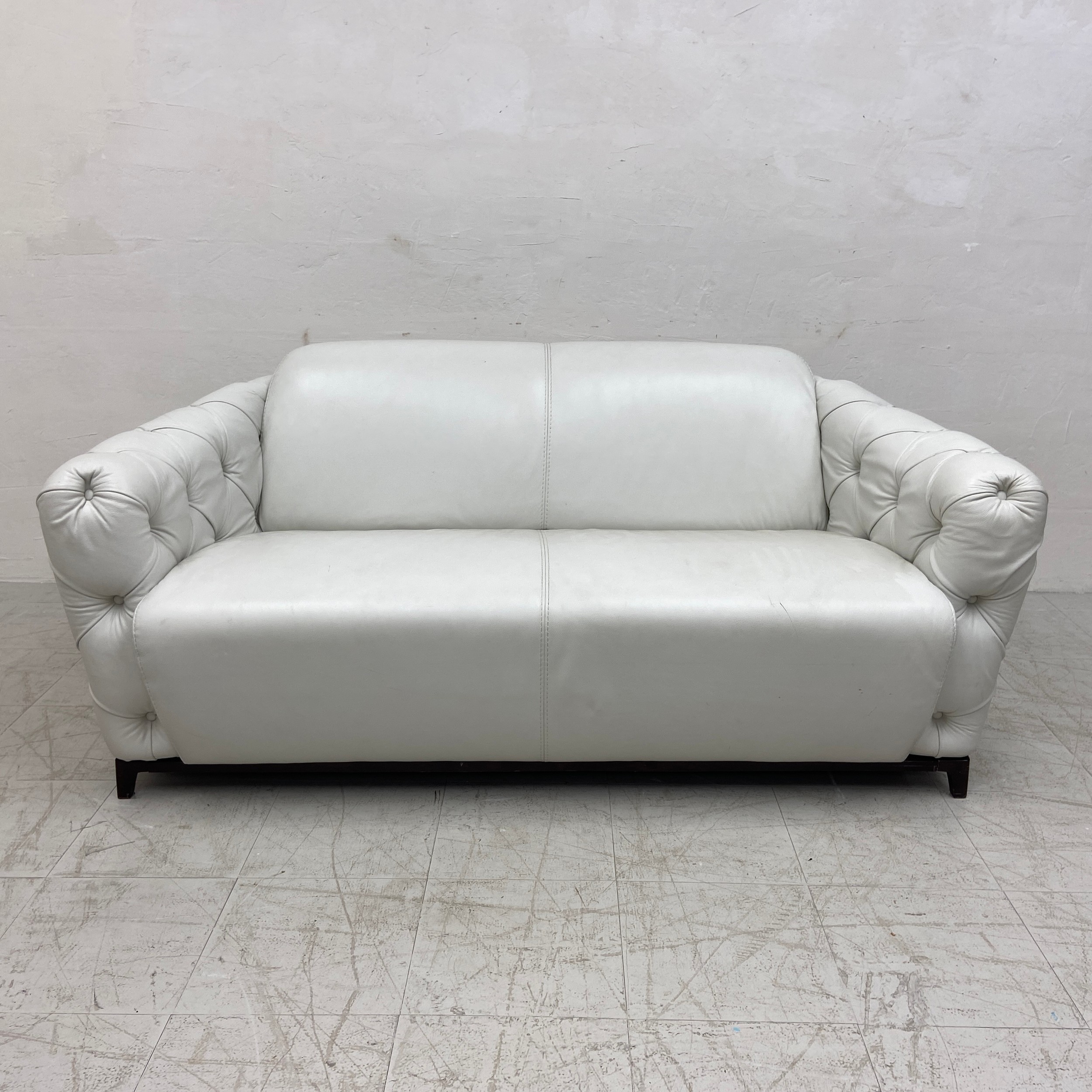A contemporary Italian white leather two seater sofa having a curved back and deep buttoned arms
